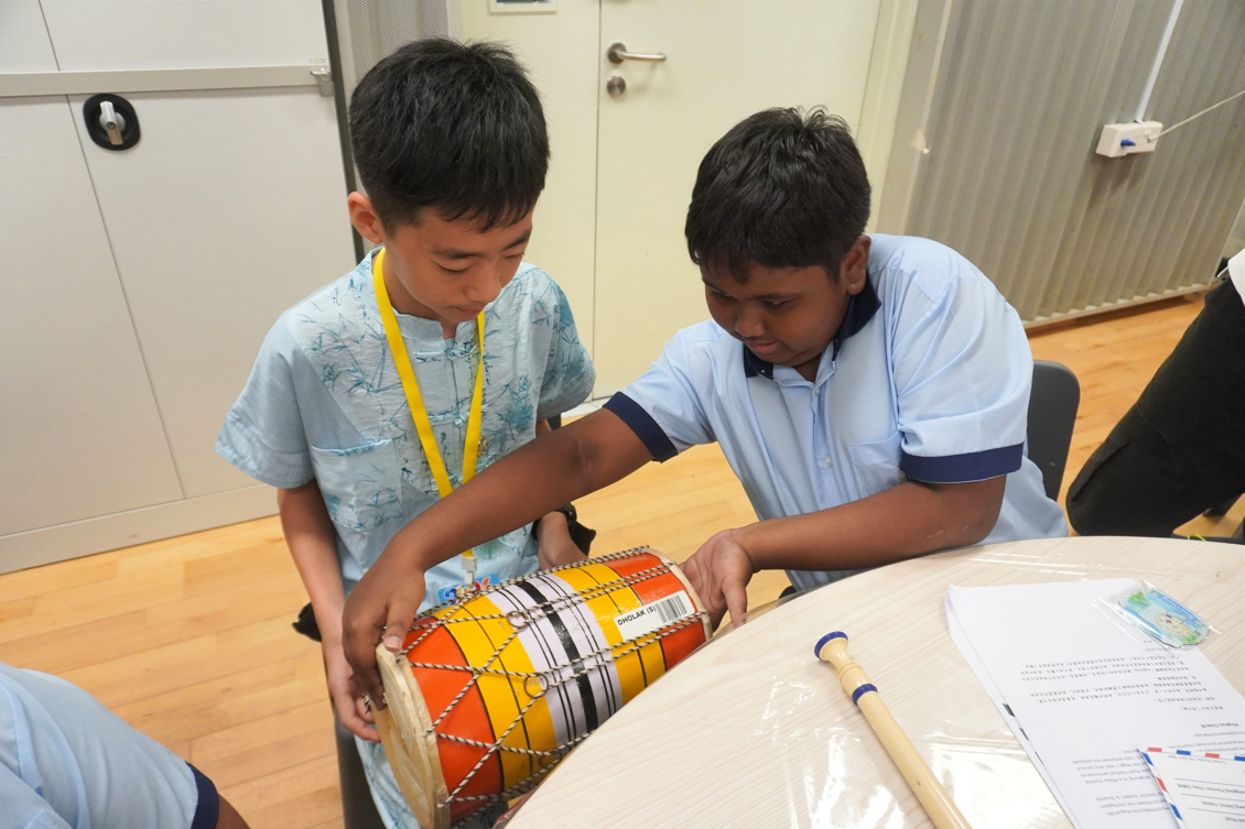 Two young boys leaning over a table to examine and play a traditional drum together.
